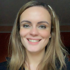 Imagem de uma mulher branca, loira de cabelos lisos, sorrindo com um fundo escuro.