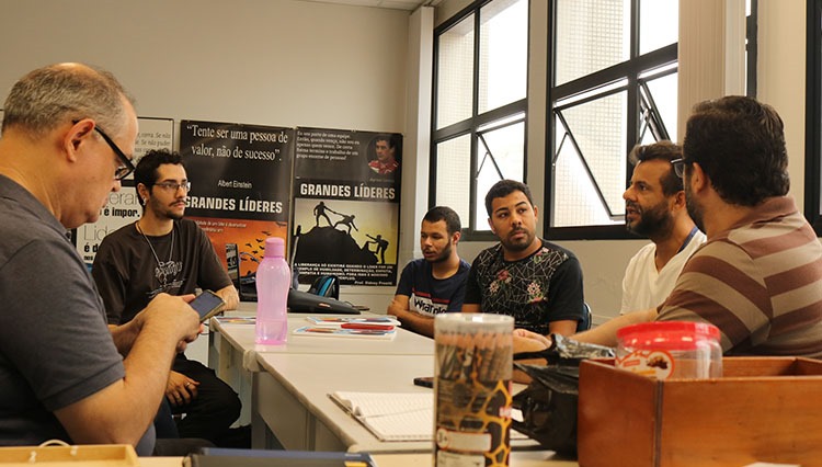 Voluntários do curso voltado a imigrantes reunidos entorno de uma mesa debatendo.