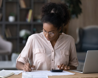 Imagem com um fundo de escritório desfocado, com uma jovem negra em uma mesa, usando óculos e uma camisa clara, fazendo anotações em um relatório.