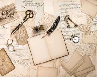 Imagem ilustrativa de papéis e objetos antigos com um caderno em branco aberto ao centro e uma pena de escrita em nanquim.
