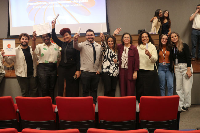 Grupo de concluintes e professores reunidos no palco, alguns segurando certificados e celebrando.