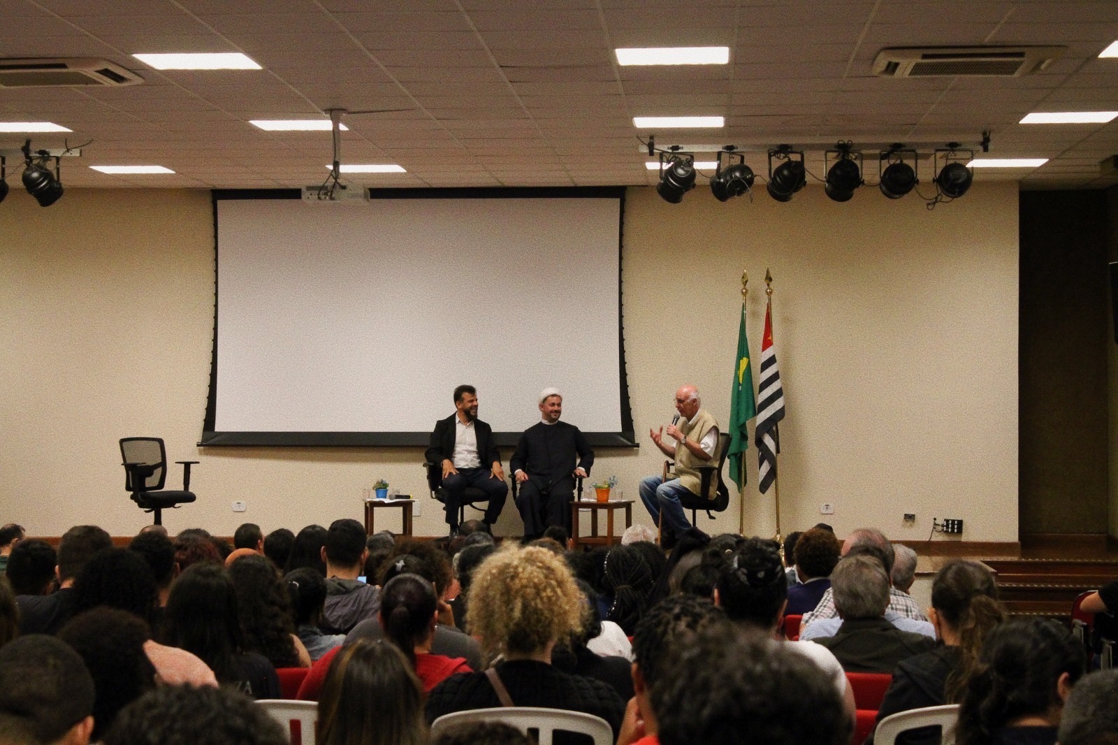 Imagem do auditório do UNIFAI, com os convidados no palco e os alunos na plateia.