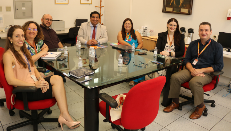 Oito pessoas reunidas na sala da reitora, sentadas, posam para foto.