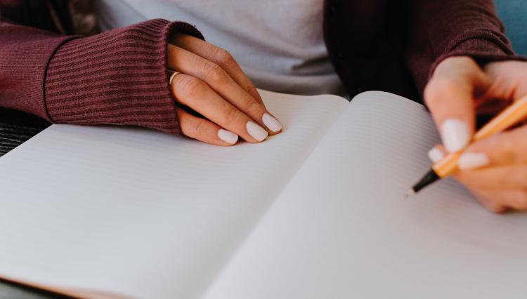 Mãos sob um caderno, segurando uma caneta