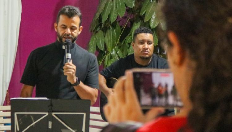 Padre Leomar, ao microfone, canta junto à aluna, para o público do sarau.