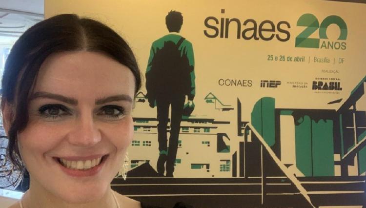 Professora Karen posa para foto em frente ao banner do SINAES